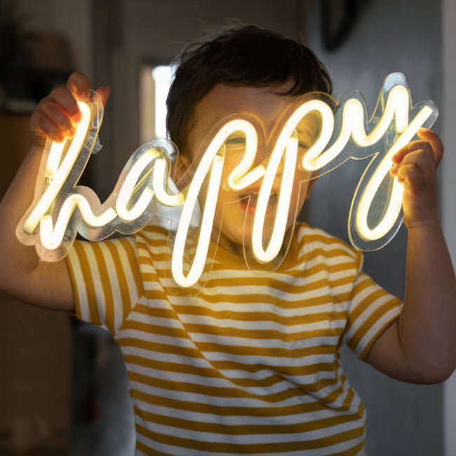 Kids room FAQ - child holding a neon sign saying "happy"